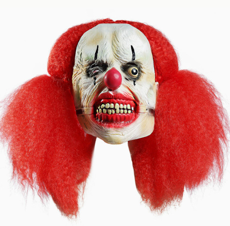 Scary clown mask with bright red hair, a pale wrinkled face, red nose and exposed teeth.