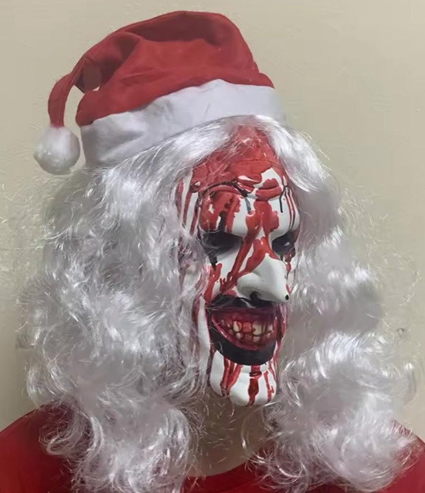 Scary pale Santa-style mask with red blood-effect markings, dark eyes and curly white hair, styled with a red Santa hat.